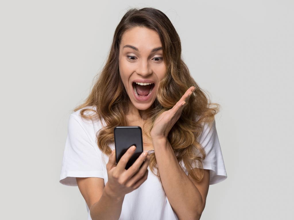 Mulher com celular na mão e expressão surpresa