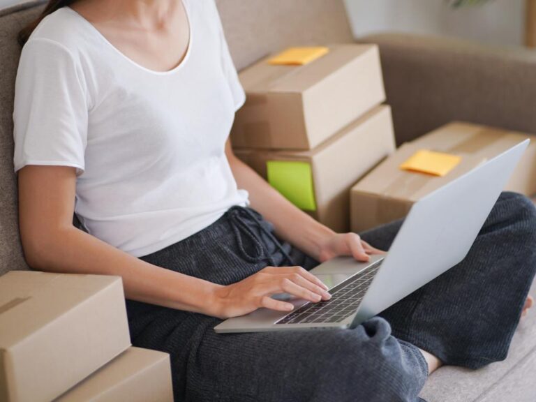 Mulher no computador com pacotes de entrega do seu lado