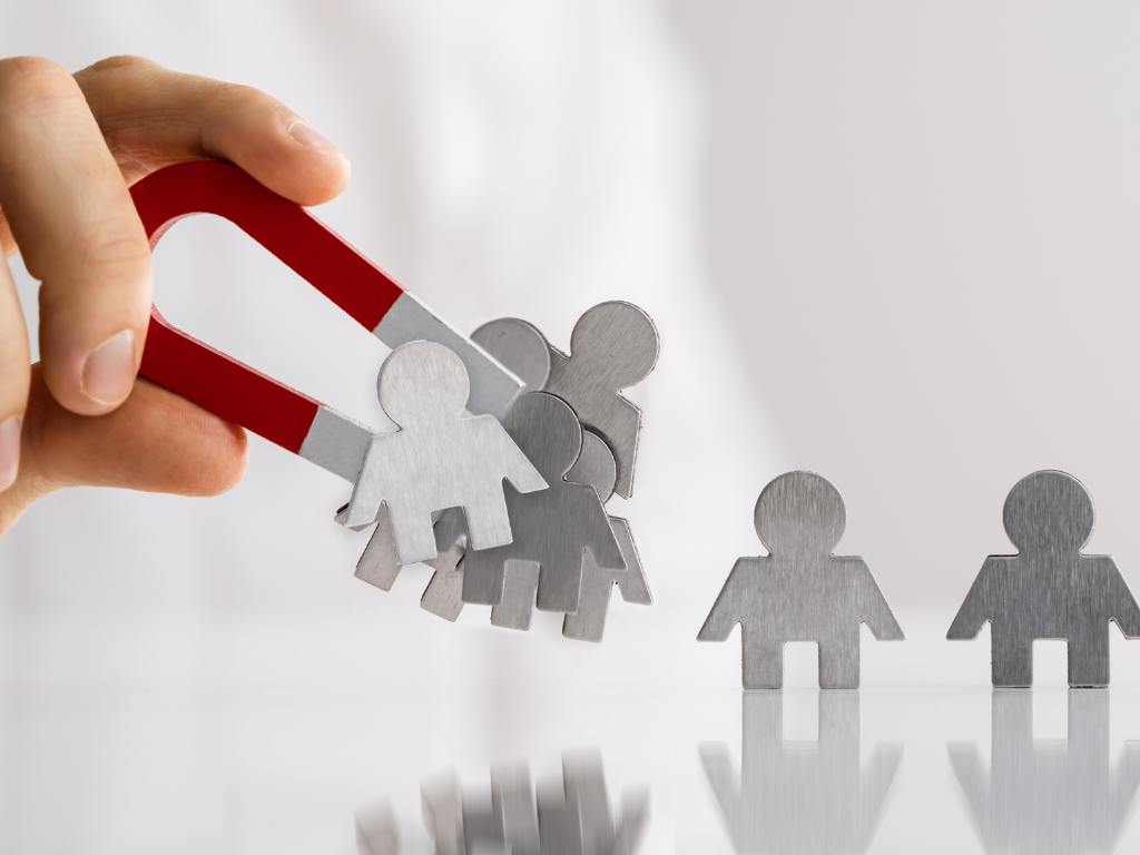 Representação de conquistar clientes, na imagem há uma mão usando um ímã puxando pessoas