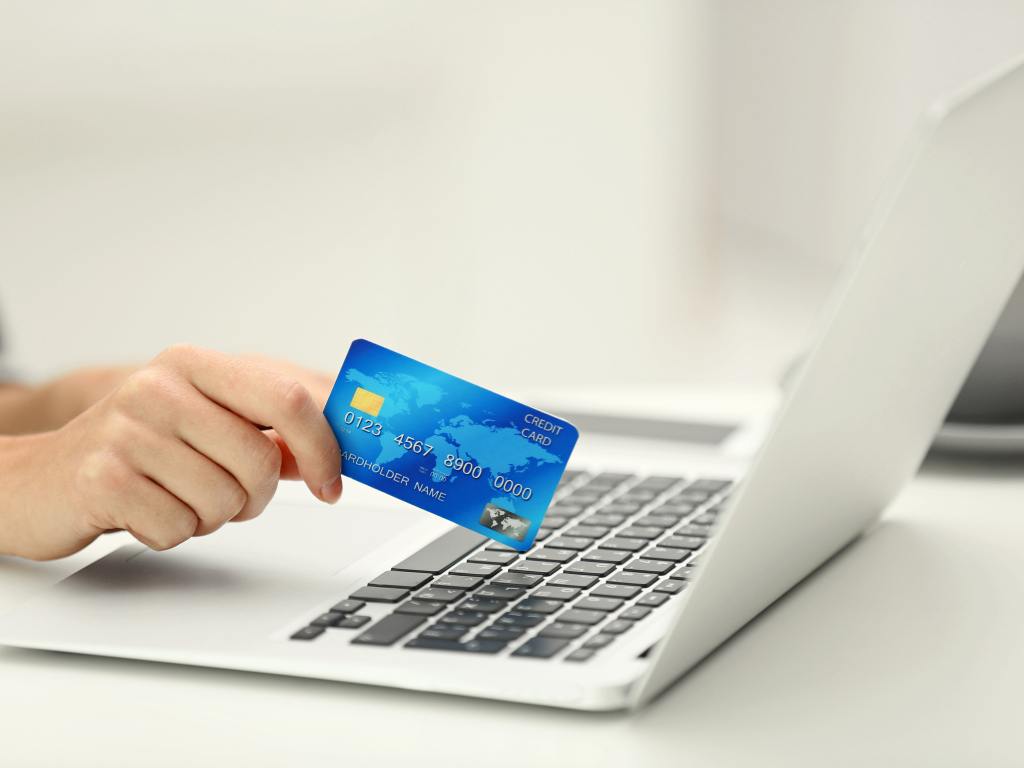 pessoa com cartão de crédito na mão usando computador