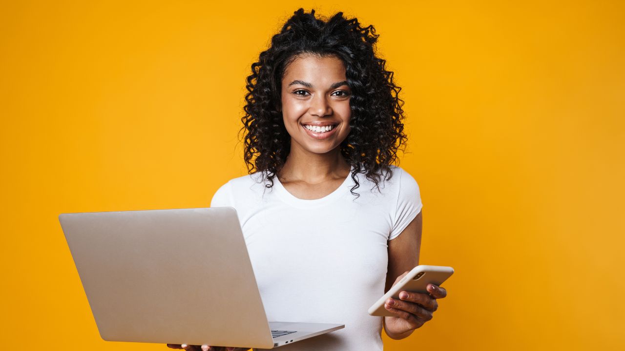 mulher sorrindo com celular e computador nas mãos